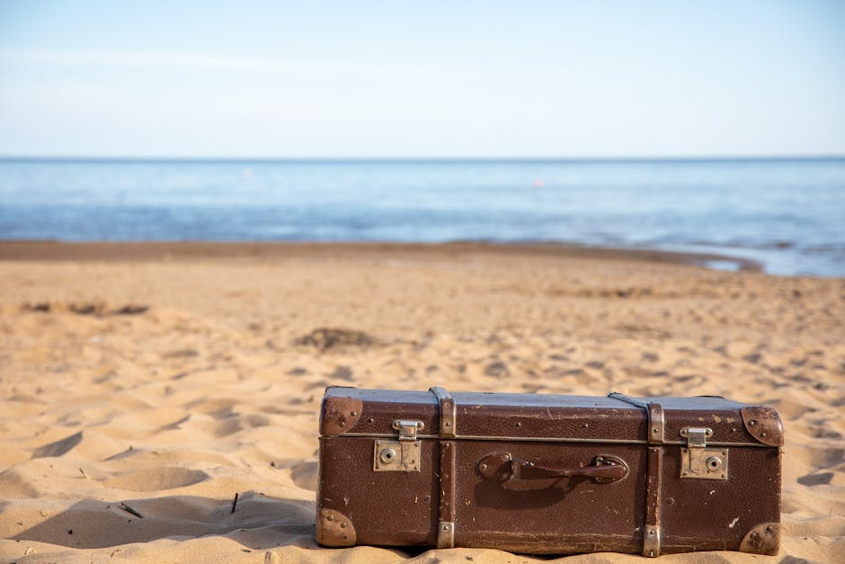 A suitcase packed with lightweight summer clothing on a sunny beach, illustrating travel packing tips for different climates