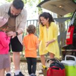 A family joyfully packing their car with luggage and snacks, excited for planning a road trip with kids